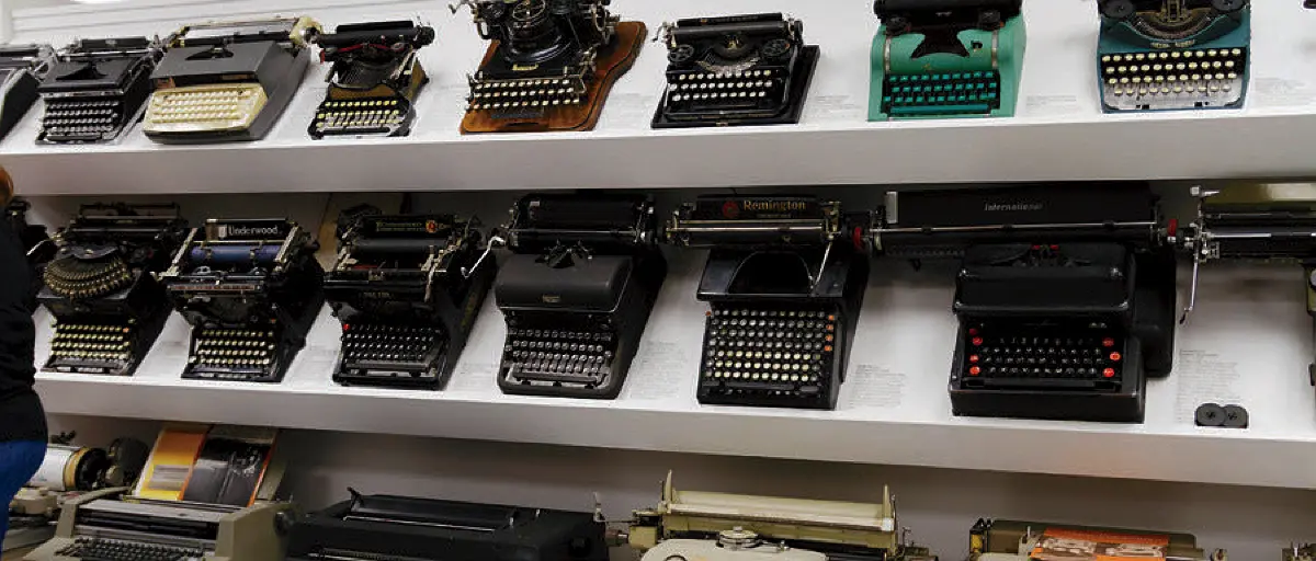Rows of vintage typewriters displayed on shelves, showcasing diverse styles and eras.