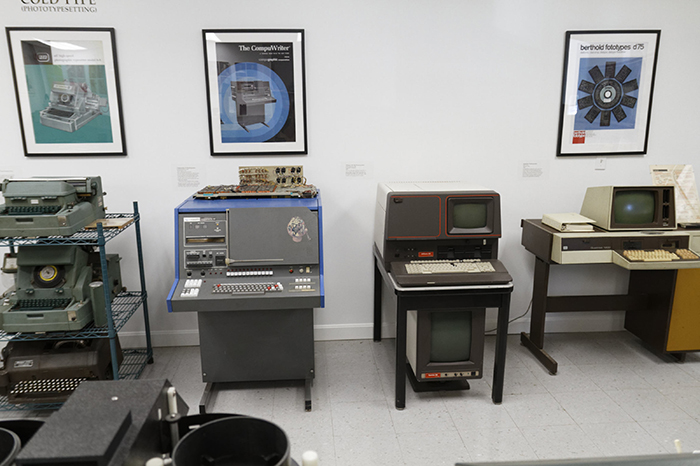 Early office machines, including computers and typesetting equipment, arranged in a museum-like setting.