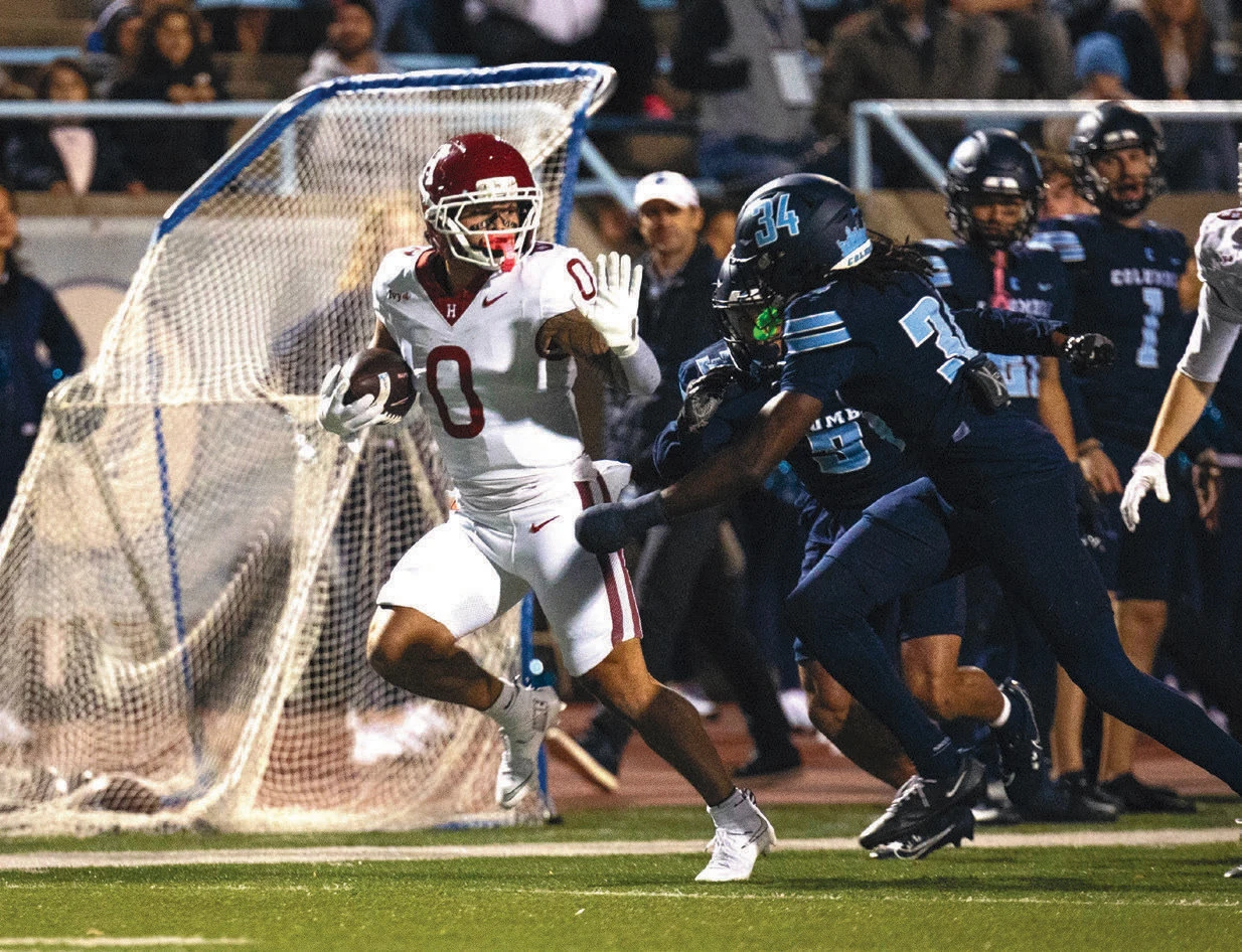 Harvard football player running with the ball while evading a tackle from a Columbia defender.