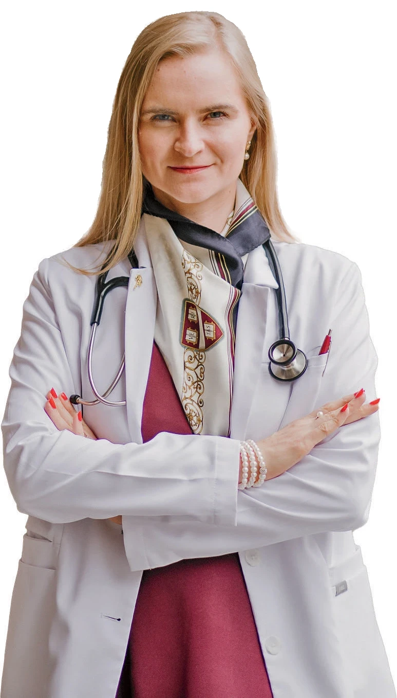Ekaterina Kostioukhina in white coat with stethoscope, pearls, and folded arms against white background.