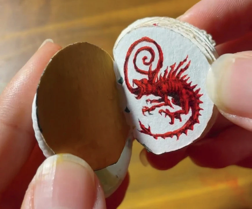 Close-up of hands holding a small circular book with a red dragon illustration inside.