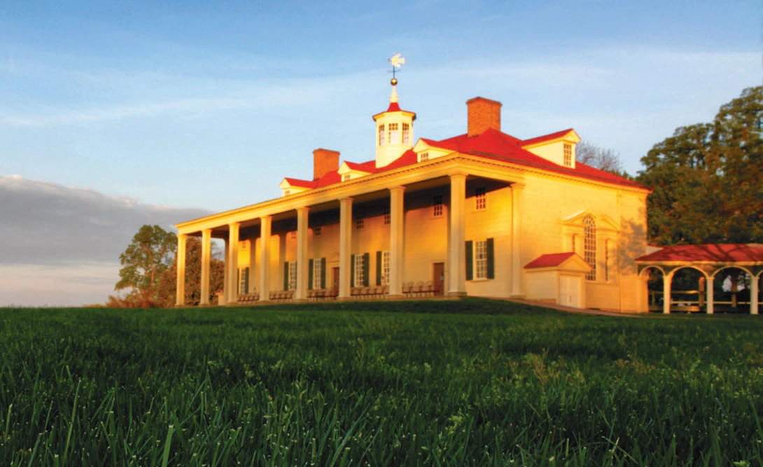 Mount Vernon plantation house with red roof and white columns lit by golden sunlight.