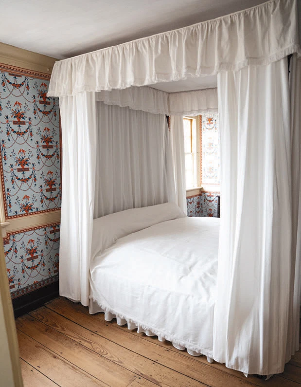 White-canopy four-poster bed in a room with floral wallpaper and wooden floorboards.