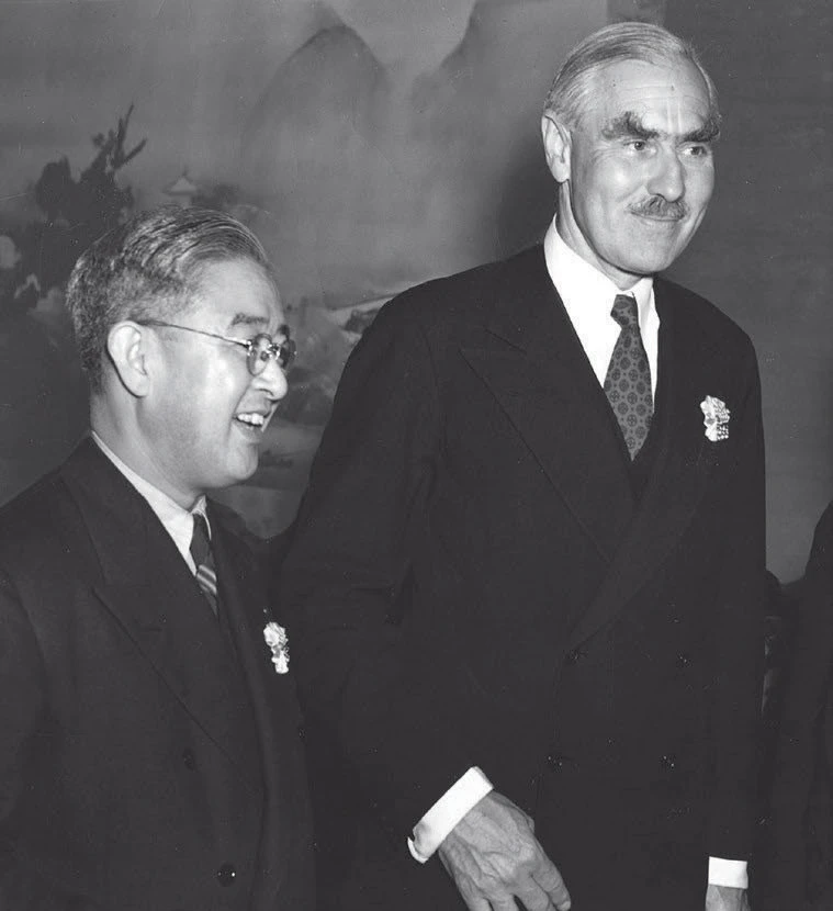 Black and white photo of two men in suits smiling at an official event or gathering.