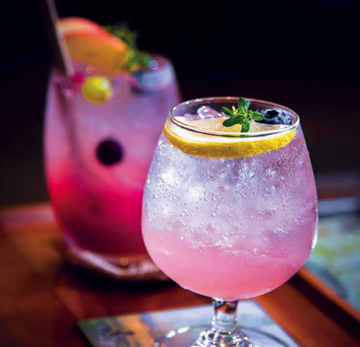 two brightly colored cocktails against a black background