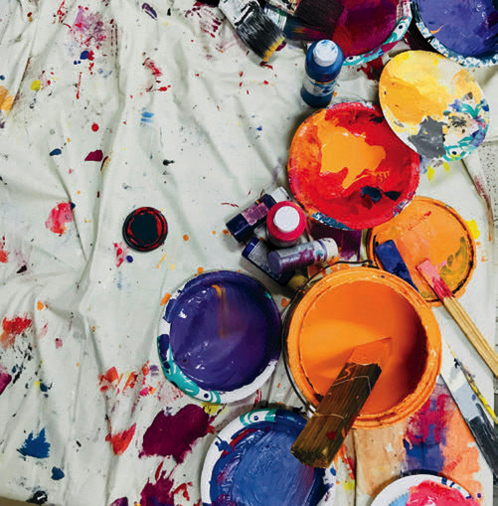 white drop cloth with containers of brightly colored paint and paint brushes