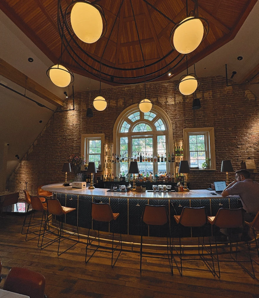 Cozy bar with brick walls, arched windows, globe lights, and leather barstools.