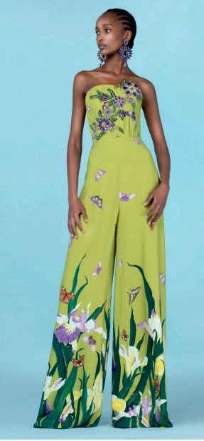 Woman wearing a strapless green jumpsuit with floral and butterfly prints, standing against a blue background.