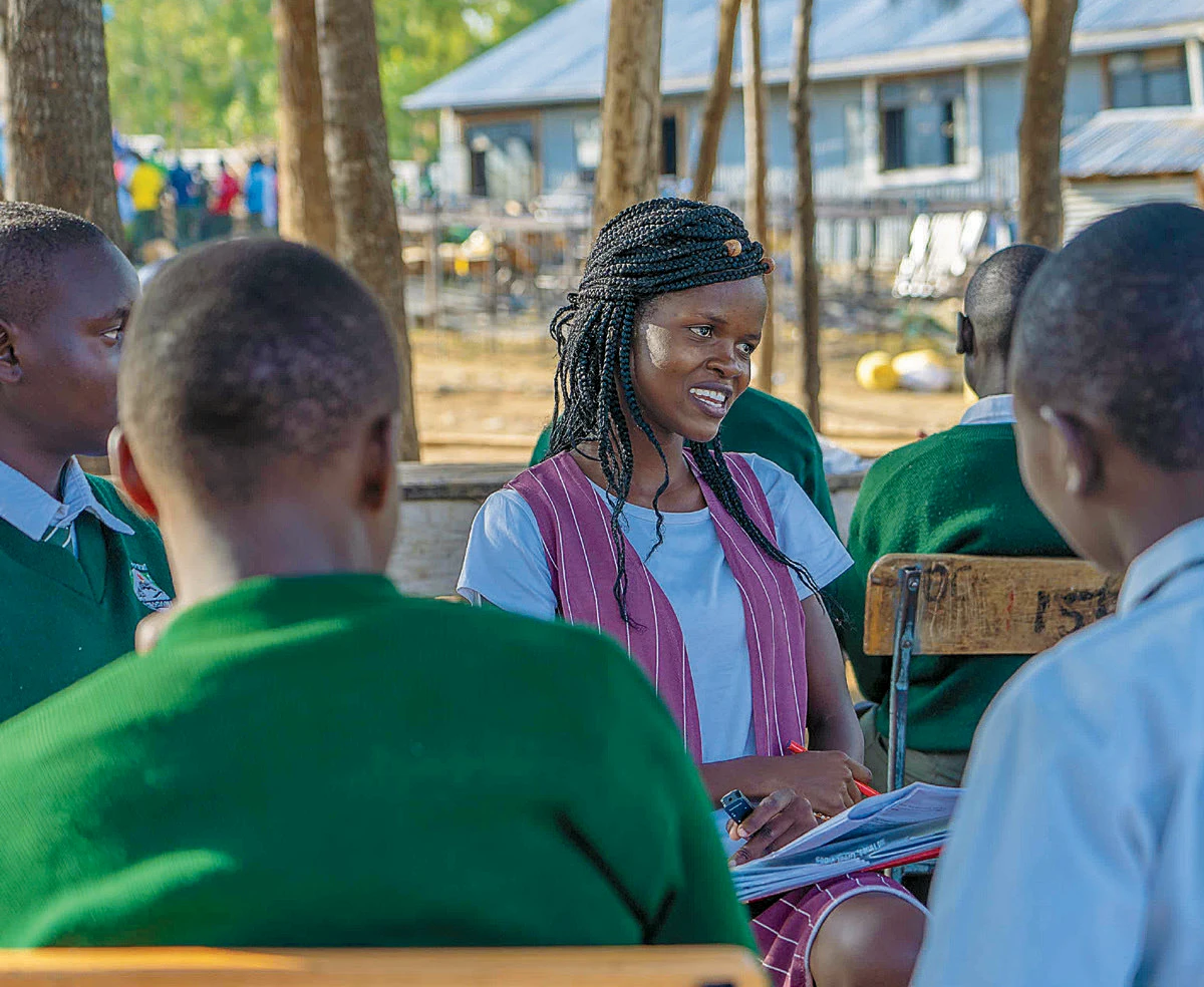 Woman leading outdoor discussion with students in green uniforms at a school setting.