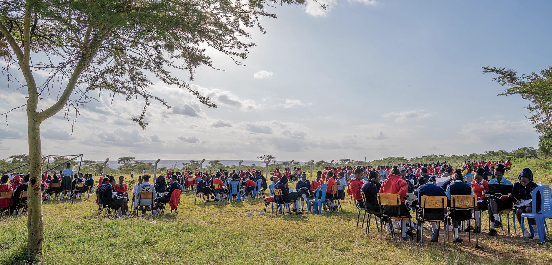 Large group of students in uniforms seated in circles outdoors, engaged in discussions under open sky.