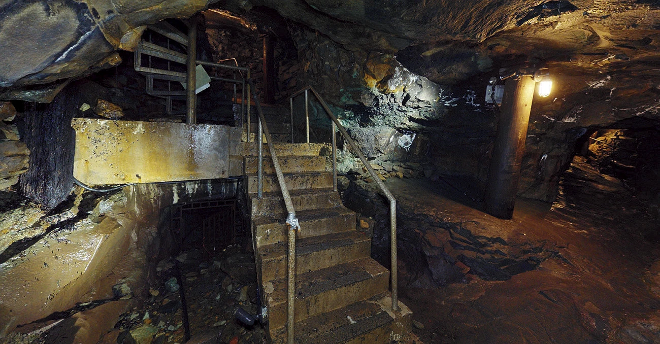 Dimly lit former copper mine tunnel with metal stairs and rocky walls.