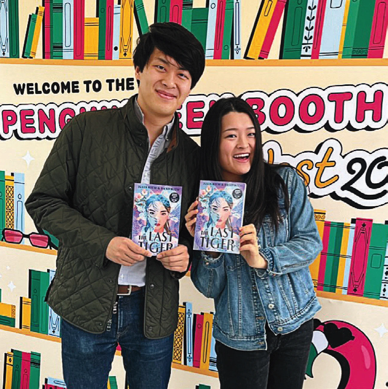 Smiling brother and sister holding copies of "The Last Tiger" in front of a colorful book-themed backdrop.
