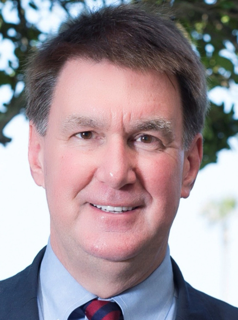 Middle-aged man in suit and tie, slight smile, greenery in background