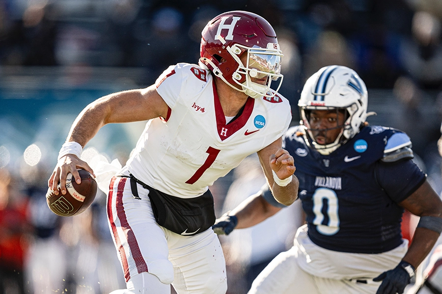 Harvard quarterback scrambles with the ball as Villanova defender closes in.