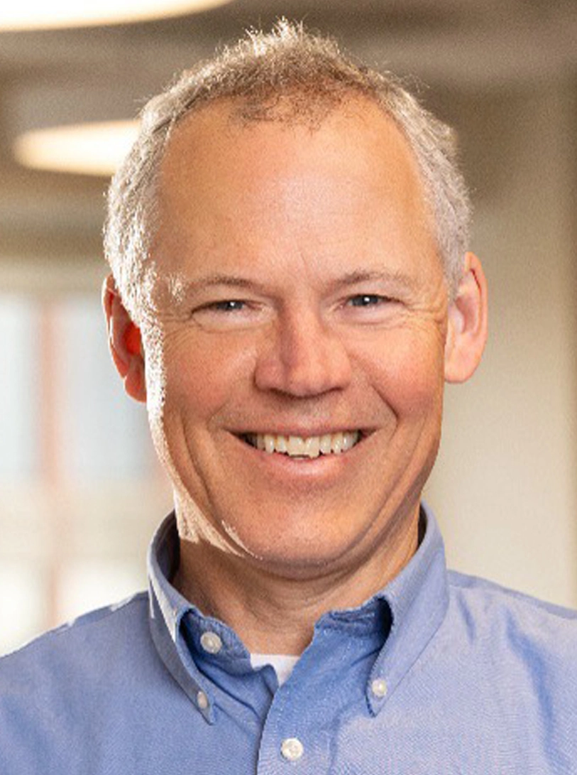 Middle-aged man with short gray hair in blue shirt, smiling in hallway
