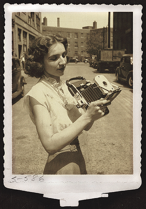 Meroë Morse holding a Polaroid Land Camera outside a building, ca. 1950s.