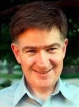 Man with short dark hair, slight smile, outdoor setting with soft blur