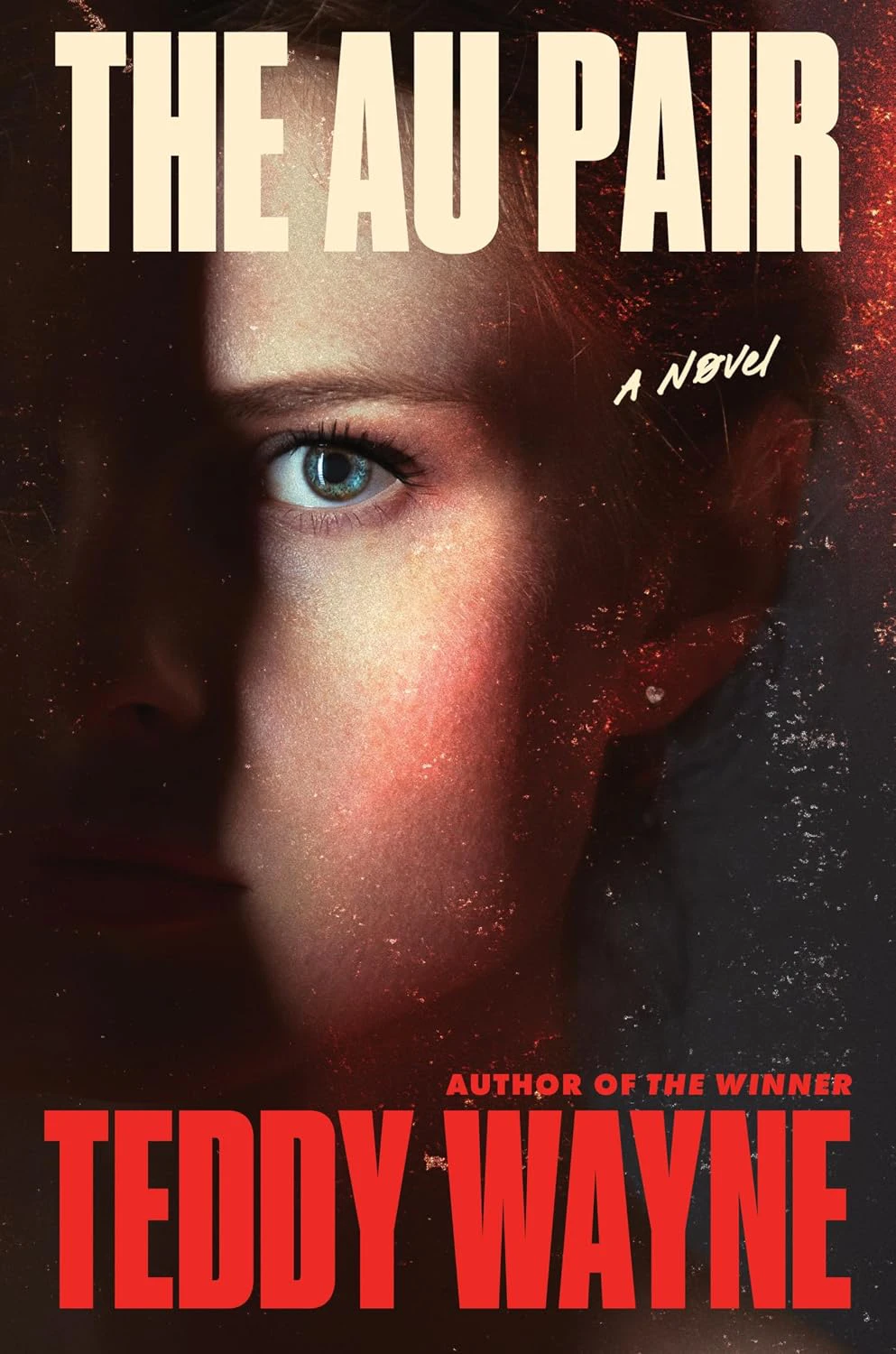 Book cover for "The Au Pair" by Teddy Wayne with a closeup of a woman's eye and face with the other half of her face in darkness