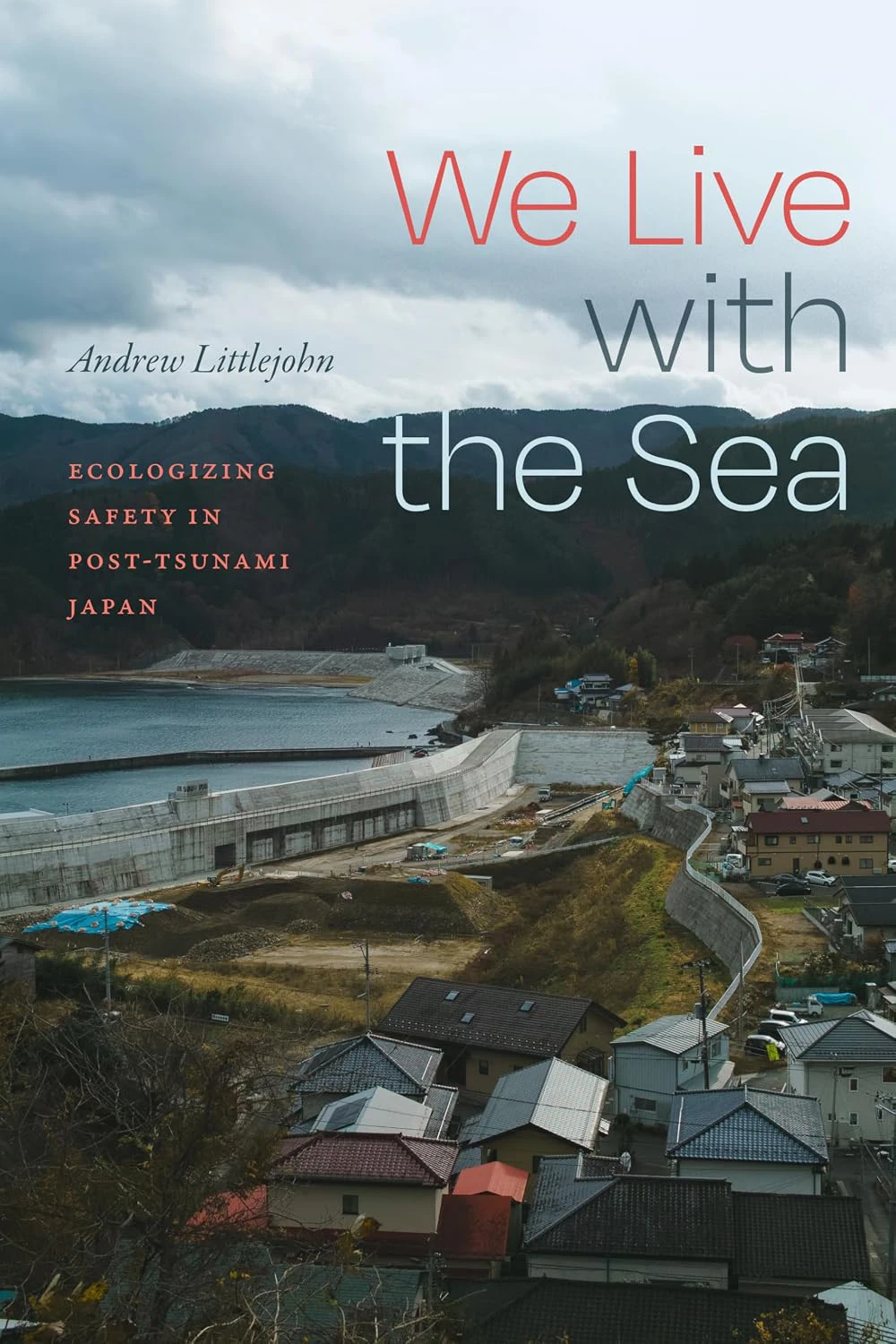 Book cover for "We Live with the Sea: Ecologizing Safety in Post-Tsunami Japan" by Andrew Littlejohn, with an image of a village with a dam and water