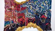 Large tapestry featuring colorful woven saris and metal bells 