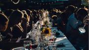 People gathered at a long, outdoor dining table set with wine glasses, candles, and flowers. 