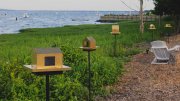 five small sculptures of houses made of brass, suspended on posts and placed on the grassy shore overlooking Duxbury Bay