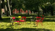 Colorful metal chairs arranged in a circle on the grass under trees in Harvard Yard. Red brick buildings in the background.