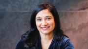 Moitri Chowdhury Savard smiling, sitting indoors against a dark background.