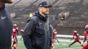 Coach Aurich on the field in Harvard Football Stadium with players in red behind him