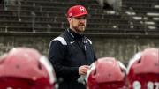 Coach Andrew Aurich standing in the center among a crowd of football players in the foreground
