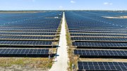 Vast solar farm with rows of solar panels under a clear blue sky.