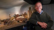 Frank Gevalt standing beside his detailed model city "Port Charles," featuring buildings, bridges, and an urban skyline.
