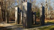 Wooden pillars with curved metal hooks arranged in an outdoor installation.