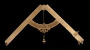 An antique brass plumb level with engraved markings, a curved scale, and a hanging plumb bob against a black background.