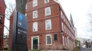 sign in the foreground reading "Massachusetts Hall" with Massachusetts Hall at Harvard University in the background