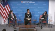 Three panelists seated on stage at the Harvard Kennedy School Institute of Politics, next to a large American flag