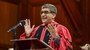 Rakesh Khurana, wearing a red doctoral robe, speaking at a podium 