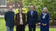 Four 2025 Centennial Medal recipients standing outdoors in a row, smiling, with greenery and a brick building behind them.