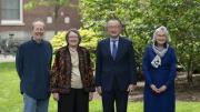 Four 2025 Centennial Medal recipients standing outdoors in a row, smiling, with greenery and a brick building behind them.