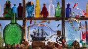 Colorful glass bottles and nautical trinkets line a window shelf, with a ship in a bottle as the centerpiece.