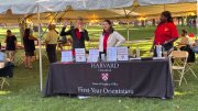 people stand at a table that reads "Harvard College Dean of Students Office First-Year Orientation"