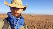 Javier Ortega-Hernández wearing a straw hat and blue scarf stands in a vast, arid landscape.