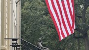 John Harvard statue and the American flag above 