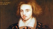 Renaissance portrait of young man thought to be Christoper Marlowe with light beard, wearing ornate black coat with gold buttons and red patterns.