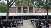 Outdoor convocation ceremony with a crowd seated under a tent, against Memorial Church