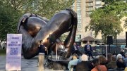 A bronze sculpture of intertwined hands in a park, with a discussion panel in the foreground.
