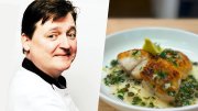 Chef standing confidently with arms crossed, alongside a plated fish dish with herbs.