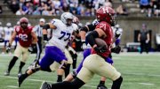 A football player in a red jersey sprints down the field, evading defenders in purple.