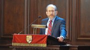 Alan Garber speaking at a podium in Memorial Church, with wooden panels in the background.