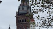 Historic building tower with intricate architecture against a gray sky, partially obscured by tree branches.
